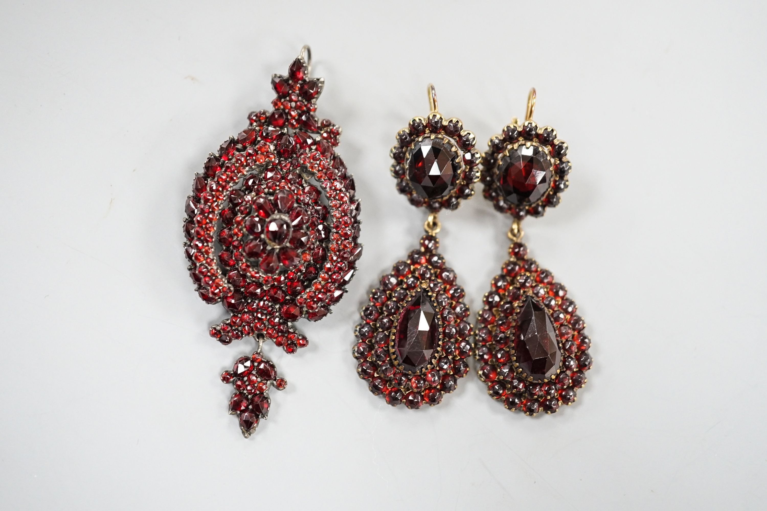 A pair of Victorian gilt metal and facet cut garnet set drop earrings, 51mm and a similar white metal and garnet set pendant brooch.